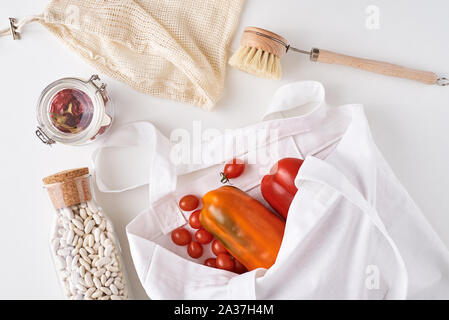 Plastic free reusable products, zero waste concept. Fresh vegetables, beans in glass bottle and textile shopping bag on white background Stock Photo