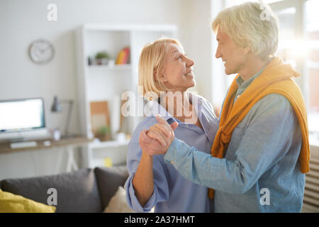 Side view portrait of happy senior couple slow dancing in living room lit by sunlight, copy space Stock Photo
