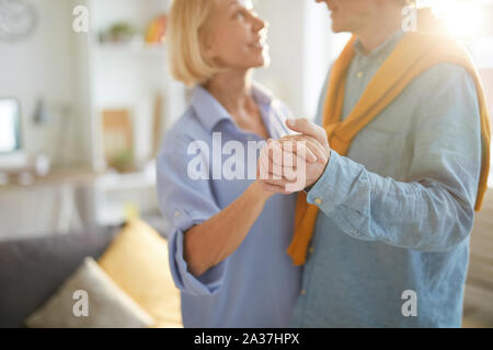 Cropped portrait of loving senior couple slow dancing in living room lit by sunlight, copy space Stock Photo