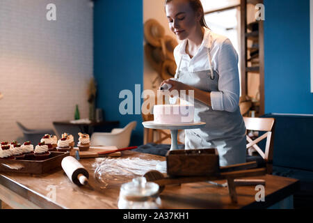beautiful pleasant woman putting cream on the cake, decoration concept. pastime concept. Stock Photo