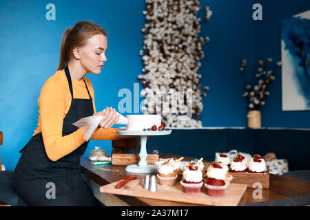 young talented female cook concentrated on decorating cke with cream. close up side view photo. profession, occupation, job Stock Photo