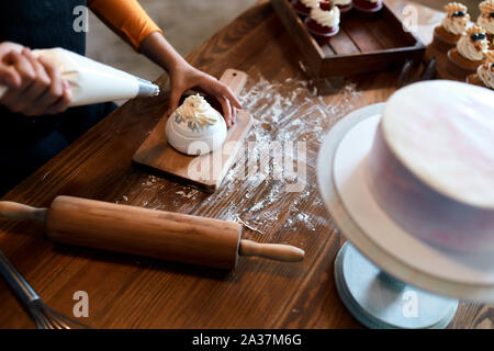 woman fillling the top of cake with white cream, close up top view cropped photo Stock Photo