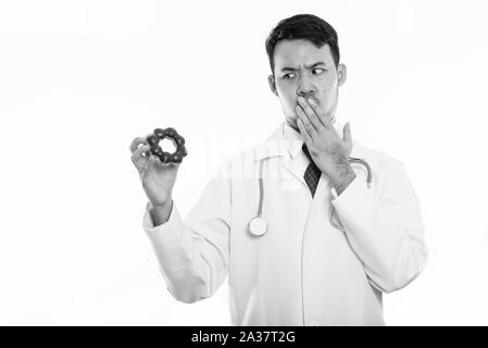 Studio shot of young Asian man doctor holding donut while looking shocked Stock Photo