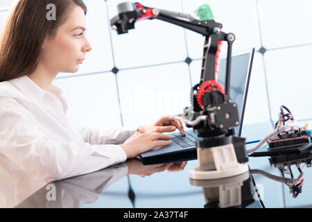 A young woman writes an algorithm for the robot arm. Science Research Laboratory for Robotic Arm Model. Computer Laboratory Stock Photo