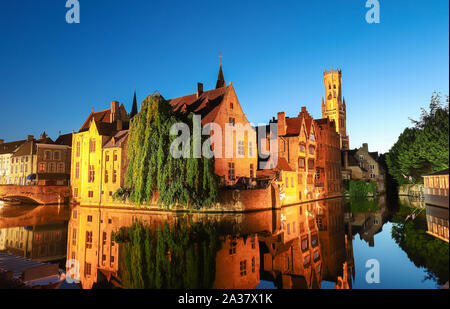 Famous view of Bruges tourist landmark attraction - Rozenhoedkaai canal with Belfry and old houses along canal with tree in the night. Belgium Stock Photo