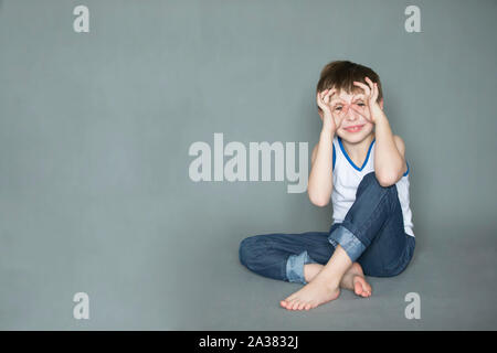 Comic happy boy holding his fingers near the eyes like glasses. Cheerful seven eight year old child. Stock Photo