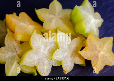 Carambola cut in stars on black ceramic plate. Exotic  starfruit  or averrhoa carambola background. Perfect  ingredient for healthy food,vegetarian or Stock Photo