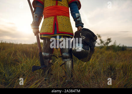 Medieval knight in armor holds axe and helmet Stock Photo