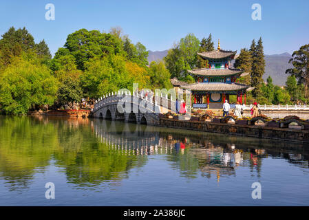 Lijiang, China - April 27, 2019: Tourists over the Suocui bridge with Moon Embracing Pavilion on the background. Stock Photo