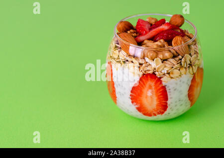 Yogurt chia pudding with fresh strawberries, overnight oats and nuts in a glass on green background. Front view. Balanced healthy breakfast concept. Stock Photo