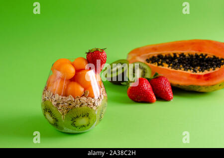Chia pudding with fresh raw tropical fruits, oat flakes for healthy eating on green background. Balanced diet breakfast concept. Front view, copy spac Stock Photo