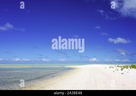 A man walks along a white sandy beach next to a turquoise lagoon on the island of Fakarava in the South Pacific Stock Photo