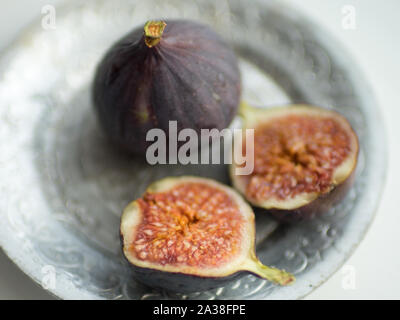 One whole fig and the second cut in half on a white table. Selective focus, closeup. Stock Photo