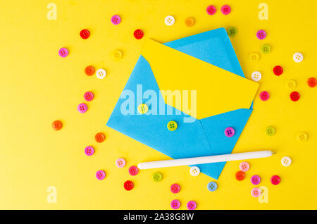 Top view of blue envelope,yellow blank card, pen and colorful buttons. Flay lay, mockup concept. Space for text Stock Photo