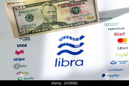 The Libra Association logo on paper brochure and US dollar banknotes. Illustrative for Facebook's global currency Libra which opposites the fiat money Stock Photo