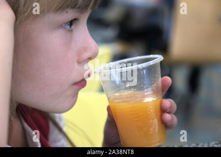 Close up of cute child girl drinking orange juice from plastic cap in a restaurant. Stock Photo