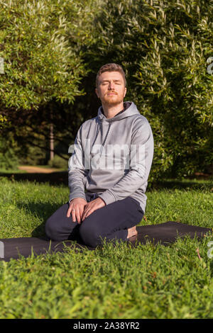 Inspired man doing yoga asanas in city park. Fitness outdoors and life balance concept. Stock Photo