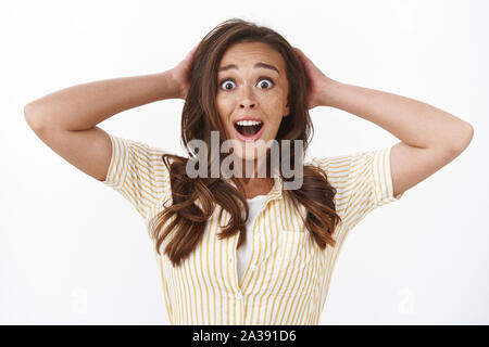 Close-up nervous surprised young woman with freckles, receive unexepected news, gasping drop jaw shocked, grab head astonished, stare camera with Stock Photo