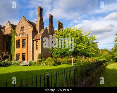 Chenies Manor House in evening sun, seen from the ha-ha across the lawn.Cut brickwork chimneys feature against a blue sky with fluffy clouds. Stock Photo