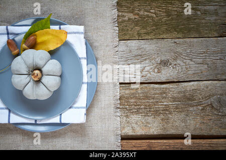Thanksgiving table setting, cement pumpkin, dry leaves and acornson gray plate on a dark wooden surface Stock Photo
