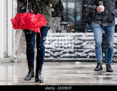 Young people walking on snowy winter city sidewalk, holding umbrella and warm drink, from waist down Stock Photo