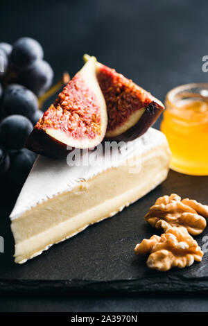 Brie cheese with figs, grapes, walnut and honey on black slate. Camembert cheese plate Stock Photo