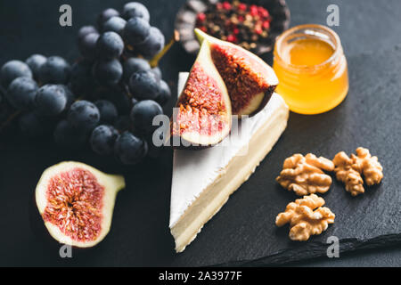 Camembert or brie cheese with figs, honey, walnuts and black grapes served on slate. Tasty cheese plate Stock Photo
