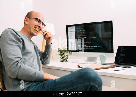 Programmer, working behind the desk, with two screens filled with code lines Stock Photo