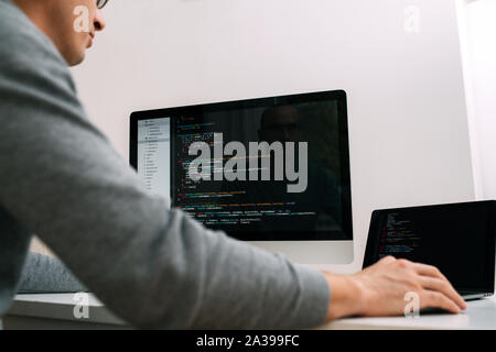 Programmer, working behind the desk, analysing code on the black screen. Stock Photo