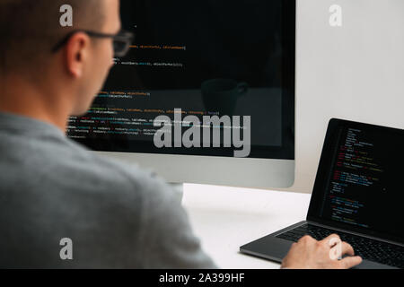 Programmer, working behind the desk, analysing code on the black screen. Stock Photo