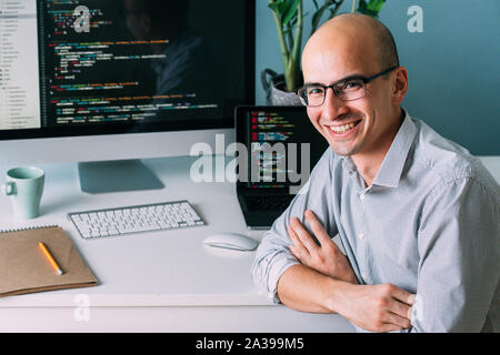 Programmer, working behind the desk, with two screens filled with code lines Stock Photo