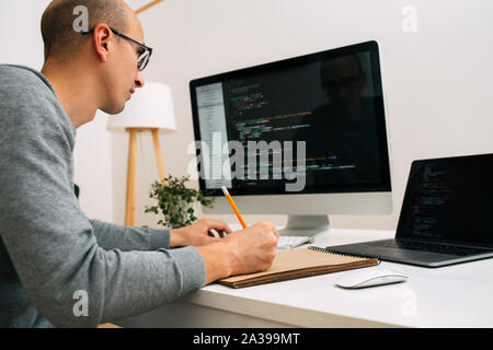 Programmer, working behind the desk, analysing code on the black screen. Stock Photo