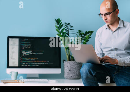 Programmer is sitting on desk, working analysing code on the laptop. Stock Photo