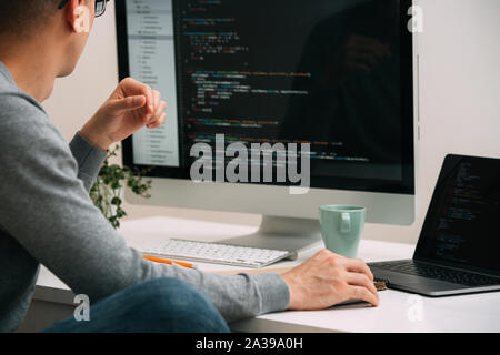 Programmer, working behind the desk, analysing code on the black screen. Stock Photo