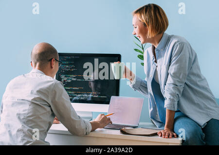 Programmer, working behind the desk, analysing code while chatting with coworker Stock Photo