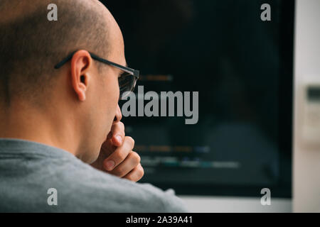 Programmer, working behind the desk, analysing code on the black screen. Stock Photo