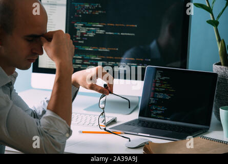 Programmer, working behind the desk, analysing code on the black screen. Stock Photo