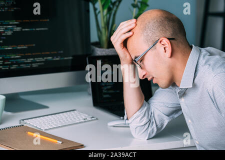 Programmer, working behind the desk, analysing code on the black screen. Stock Photo