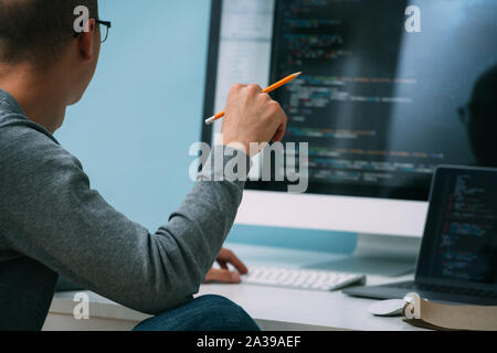 Programmer, working behind the desk, analysing code on the black screen. Stock Photo