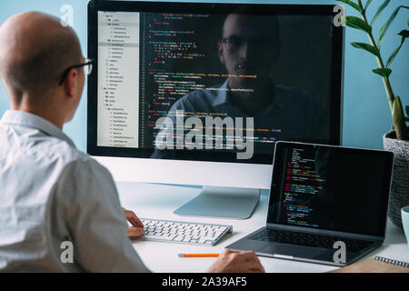 Programmer, working behind the desk, analysing code on the black screen. Stock Photo