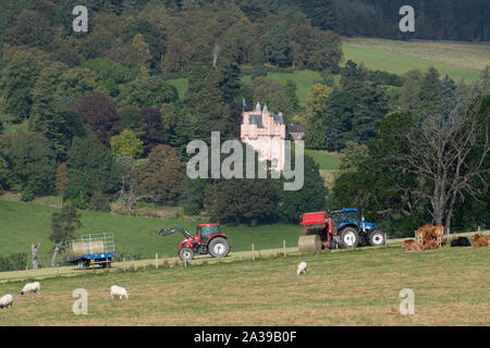 A Tractor and Baler Deposit a New Bale of Hay as a 2nd Tractor Loads Bales onto a Waiting Bale Trailer in Front of Craigievar Castle in Aberdeenshire Stock Photo