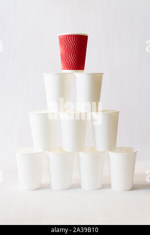 Red paper coffee cup stands on top of white paper cups pyramid. White background, copy space, vertical orientation Stock Photo