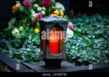 Grave light with burning candle on a grave with flowers on an autumn evening Stock Photo