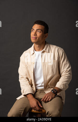 thoughtful handsome mixed race man in beige shirt looking away on black background Stock Photo