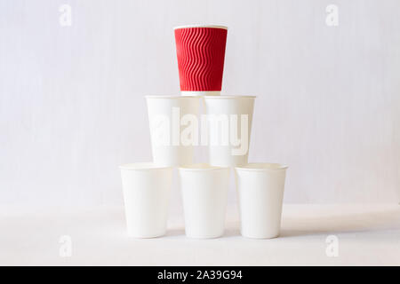 Red paper coffee cup stands on top of white paper cups pyramid. White background, copy space Stock Photo