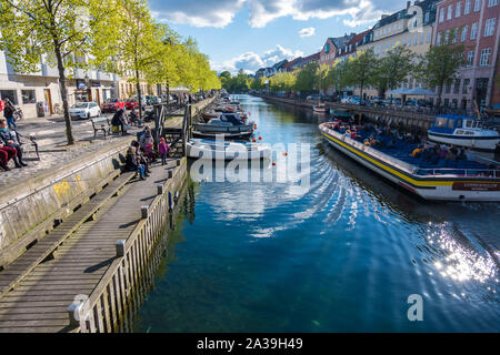 Copenhagen, Denmark - May 04, 2019: People relax on the waterfront while others explore Copenhagen on a tourist boat