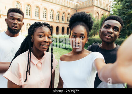 Four international students with beaming smiles are posing for selfie shot in campus Stock Photo