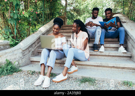 Happy students sitting on stairs in park Stock Photo