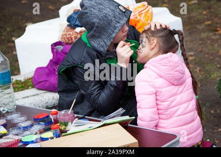 Chisinau, Moldova - October 5, 2019: Young woman painting face of kid outdoors. baby face painting Stock Photo