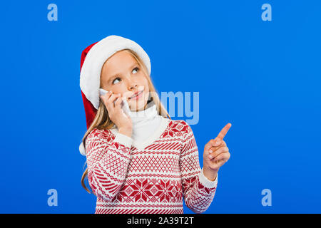 kid in santa hat and sweater talking on smartphone isolated on blue Stock Photo